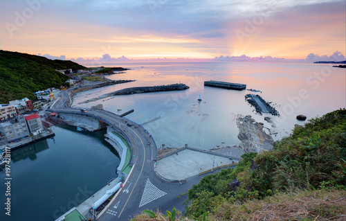 Aerial view of a fishing village at dawn on northern coast of Taipei Taiwan ~ Scenery of a coast highway along beautiful coastline and across the harbor of a fishing village under dramatic rosy sky