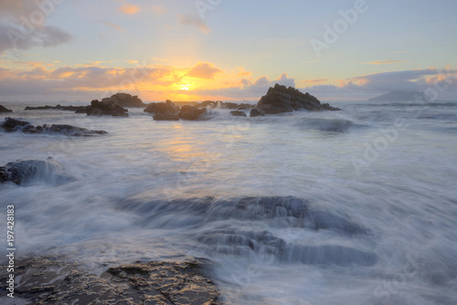 Golden rays of the rising sun light up the rocky beach at Wai'ao, Yilan, Taiwan (Long Exposure Effect)~ Scenery of a beautiful beach illuminated by the first rays of morning sunshine at Ilan, Taiwan 