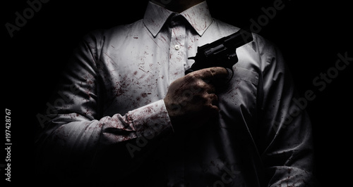 Horror scary photo of a killer in white shirt with blood splatter and posing with black gun on dark background. photo