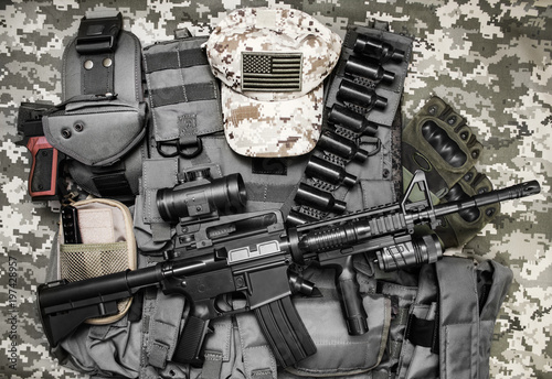 Photo of a tactical vest, rifle, gun, hat with american flag badge and cartrige belt laying on camouflage background. photo