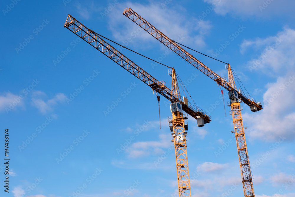 Two yellow construction cranes against blue sky with a few clouds - development in the city- copy space, design element Two yellow construction cranes against blue sky with a few clouds - development in the city- copy space, design element