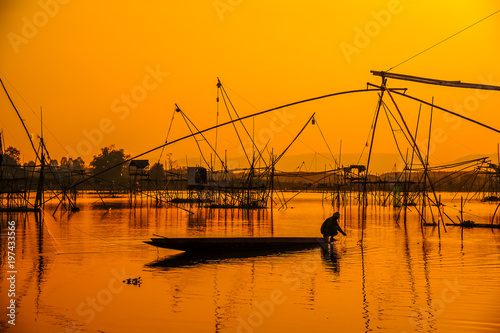 Silhouette fisherman on boat fishing by using traditional net fishing tools in swamp