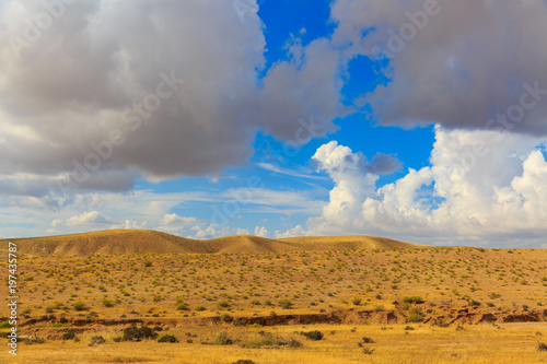 Far hills in desert under clouds in blue sky
