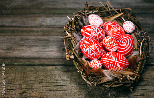 Easter red eggs with folk white pattern inside bird nest on right side of rustic wood background. Ukrainian traditional eggs pisanka and krashanka photo