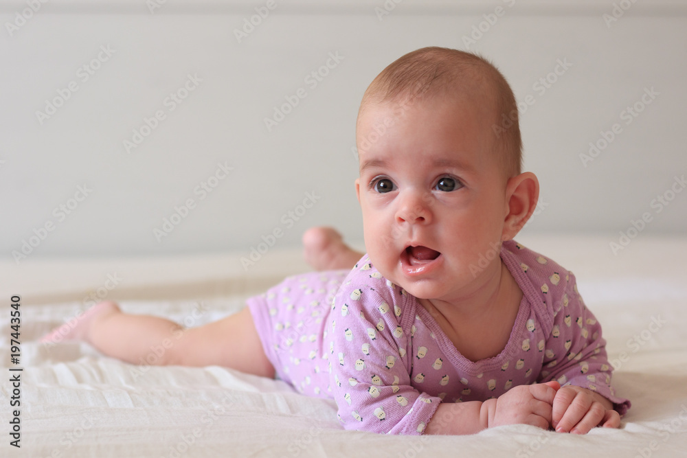 Little baby girl in white sunny bedroom, lying on the bed