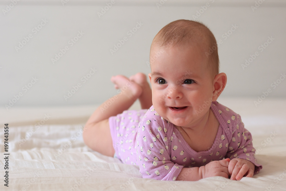 Adorable baby girl in white sunny bedroom, smiling on camera