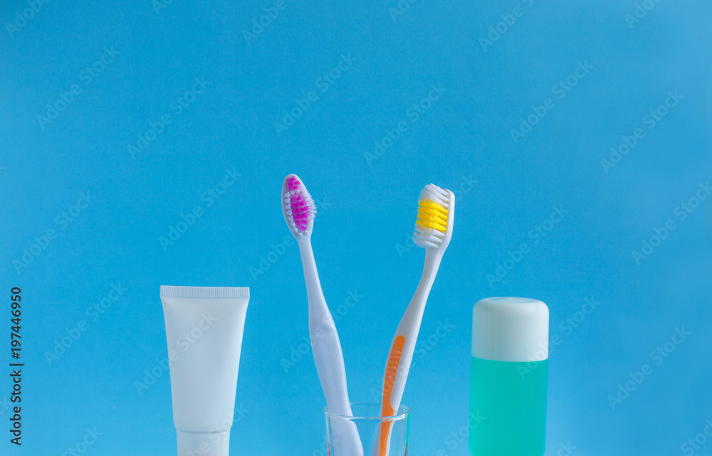 Two toothbrushes in a glass near the toothpaste and rinse against a blue background. The concept of dentistry and health. Free space for copying. Two toothbrushes in a glass near the toothpaste and rinse against a blue background. The concept of dentistry and health. Free space for copying.