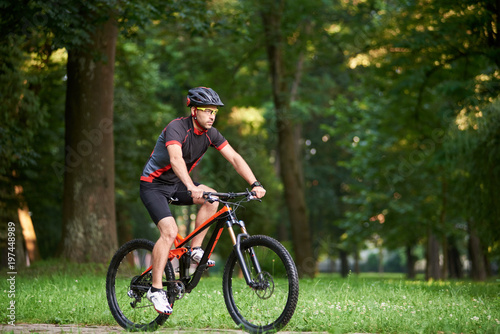 Man biker in cycling clothing and protective helmet training on bicycle, getting ready for race in park on fresh air. Man enjoying morning bike ride. Concept of motivation, healthy lifestyle
