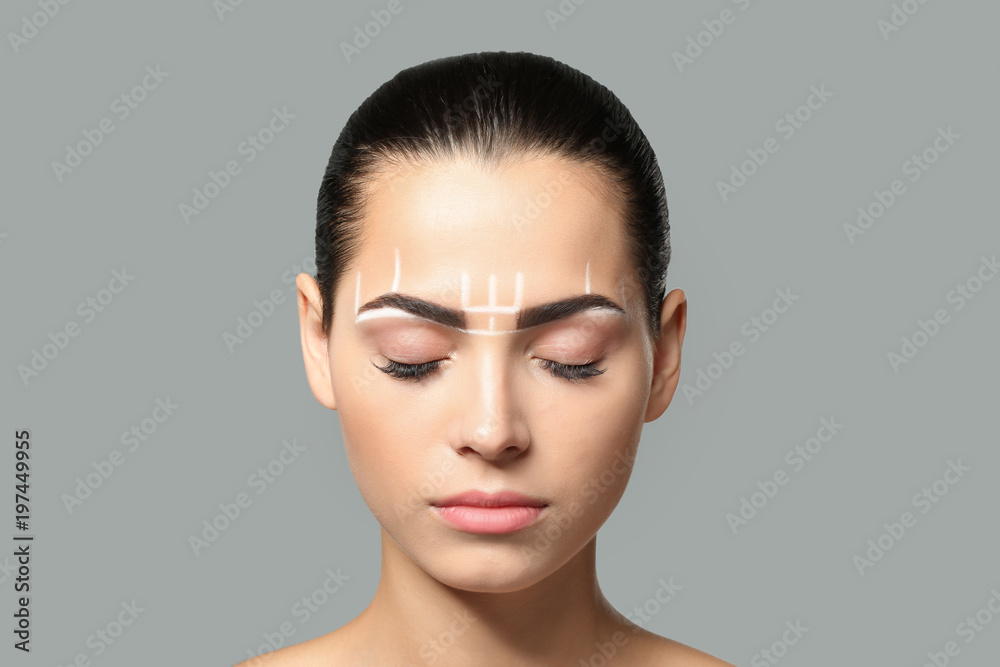 Fototapeta premium Młoda kobieta przed procedurą makijażu permanentnego brwi na szarym tle