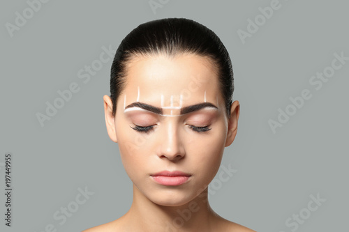 Young woman before procedure of eyebrows permanent makeup on grey background