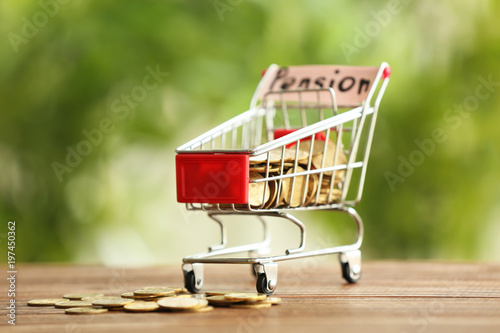 Shopping cart and coins on table against blurred background. Pension planning concept