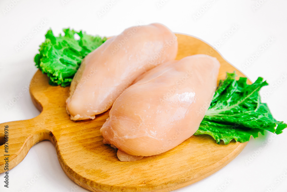 Raw chicken fillets on wooden cutting board with lettuce leaves, on white background Raw chicken fillets on wooden cutting board with lettuce leaves, on white background