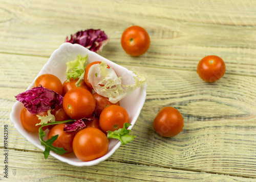 Cherry tomatoes in a white plate on a wooden background.
