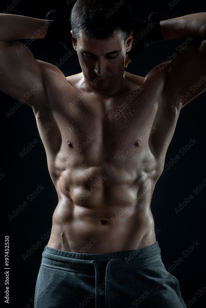 A man with a naked sports body strains the press on a black isolated background. A man with a naked sports body strains the press on a black isolated background.