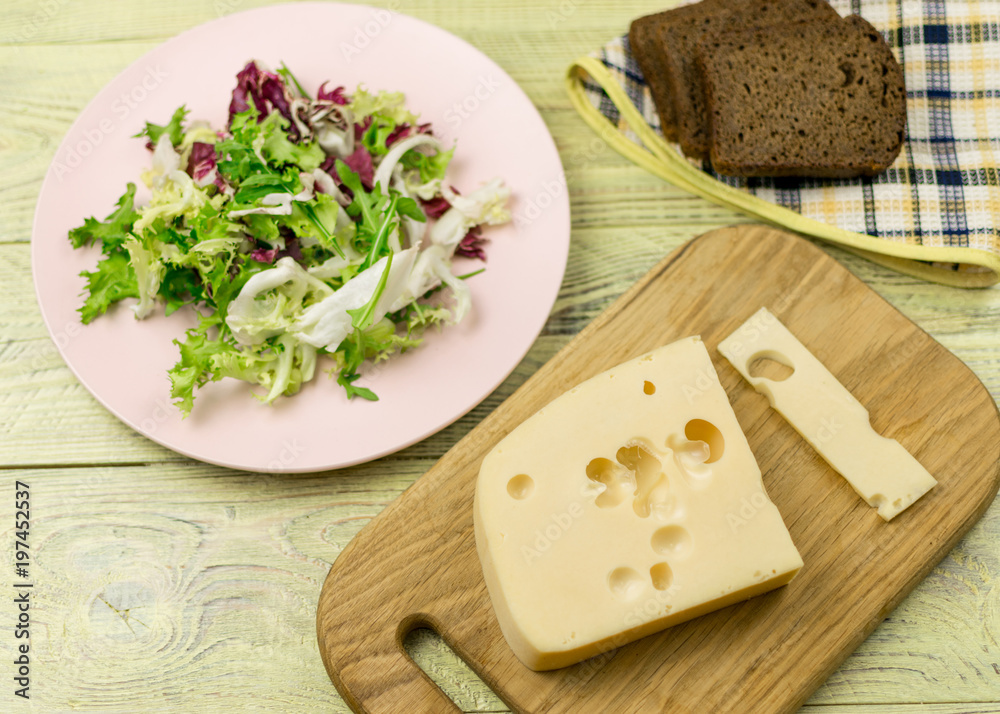 A piece of cheese and fresh vegetables next to a wooden surface. Preparation of a vegetarian salad.