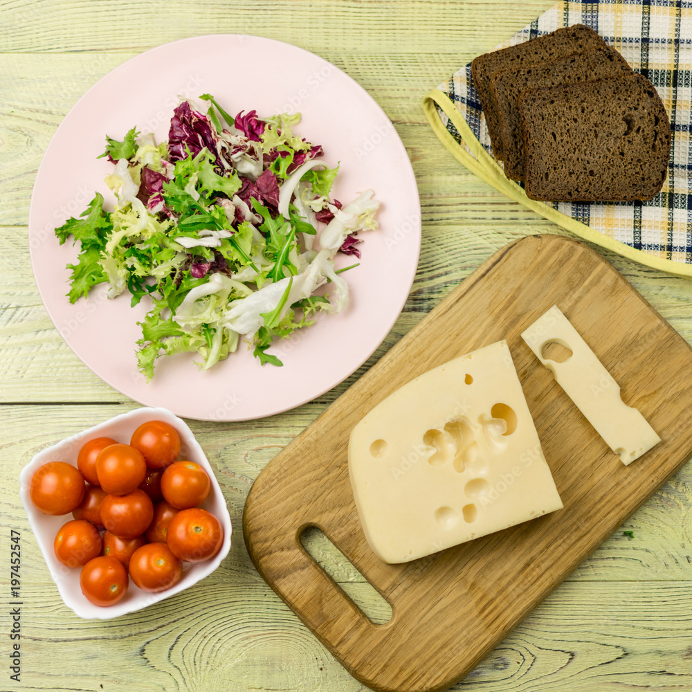 A piece of cheese and fresh vegetables next to a wooden surface. Preparation of a vegetarian salad. A piece of cheese and fresh vegetables next to a wooden surface. Preparation of a vegetarian salad.