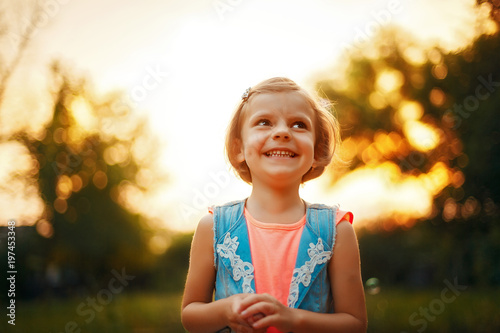 Photos Five years old caucasian child girl with fair hair looking away and smiling outdoor at sunset