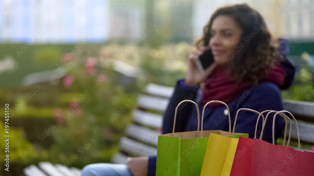 Closeup of shopping bags, woman boasts about purchases over phone on background
