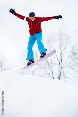 Picture of sports man in helmet with snowboard jumping in snowy resort