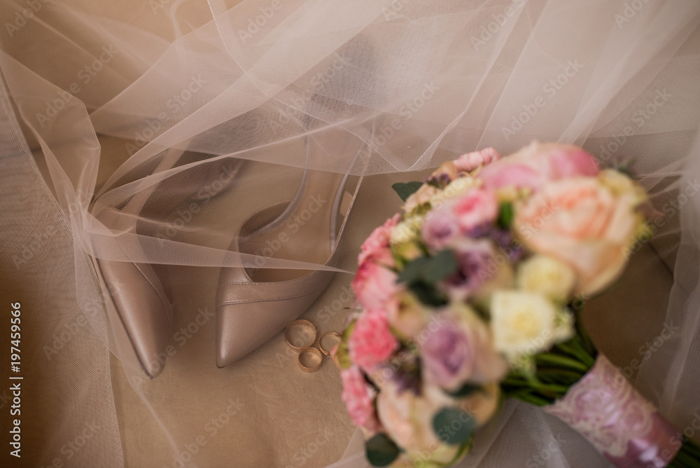 Golden wedding heels and golden rings in focus on brown background with bridal shoes, perfume and flowers out of focus. Golden wedding heels and golden rings in focus on brown background with bridal shoes, perfume and flowers out of focus.