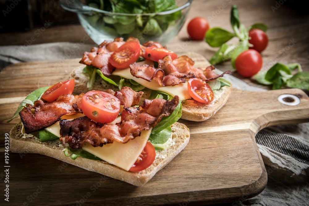 Ciabatta sandwich with arugula salad, bacon and yellow cheese.
