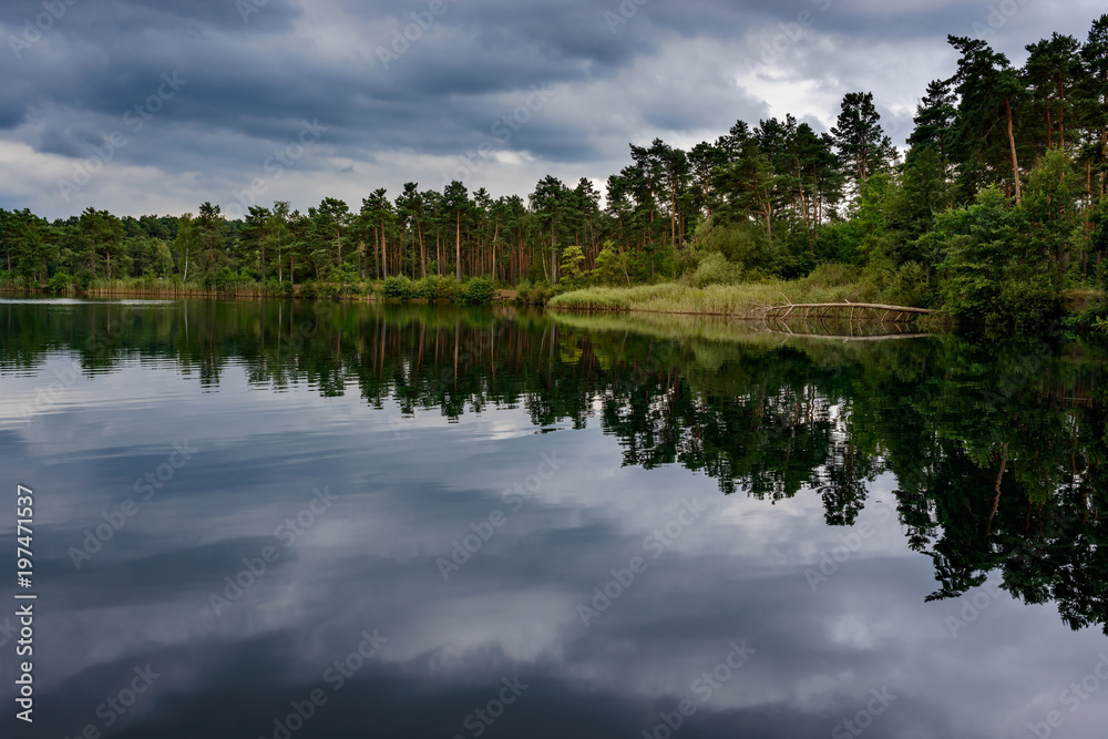 Ein dramatischer Wolkenhimmel spiegelt sich im Tonsee im Naturpark Dahme-Heideseen bei Groß Köris