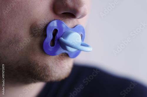 A young man holds a pacifier in his mouth