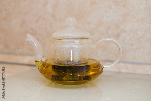 Glass teapot with blooming tea flower inside against wooden