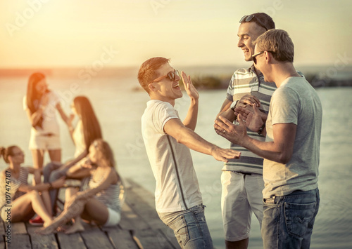 Friends sitting on wooden pier under sunset light.