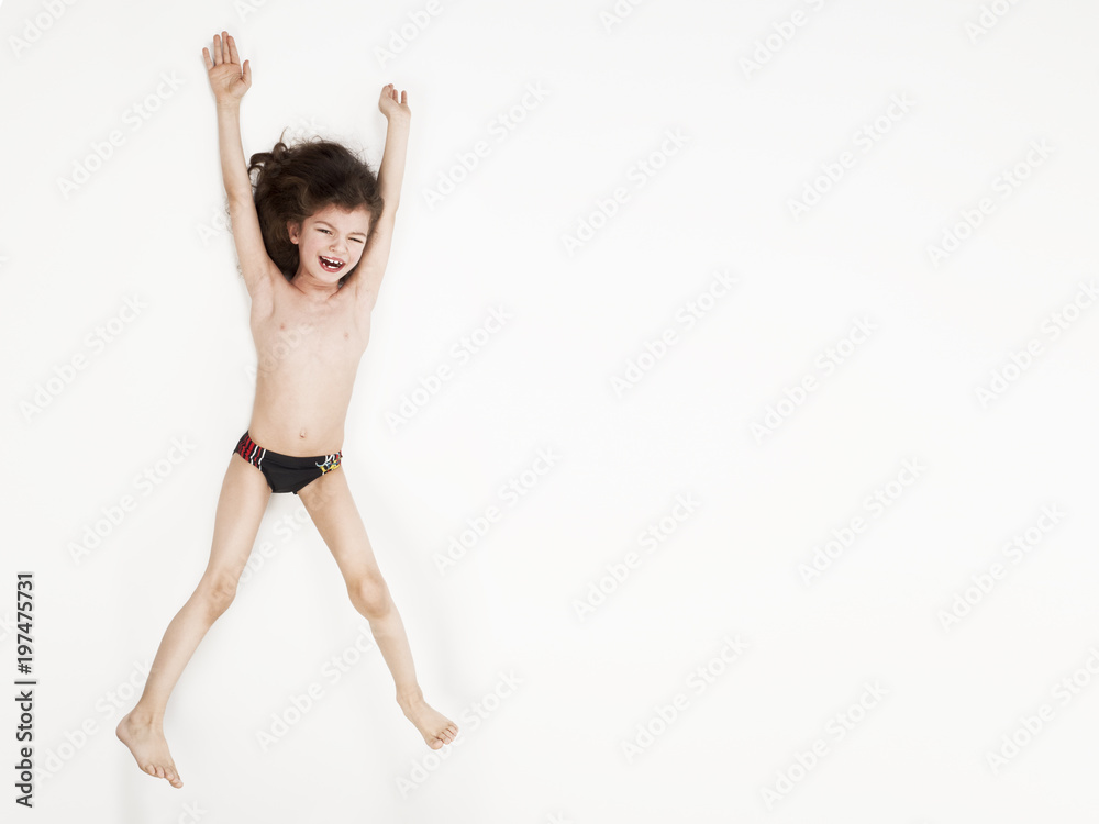 Smiling little boy in swimming trunks jumping with arms raised against a white background Smiling little boy in swimming trunks jumping with arms raised against a white background