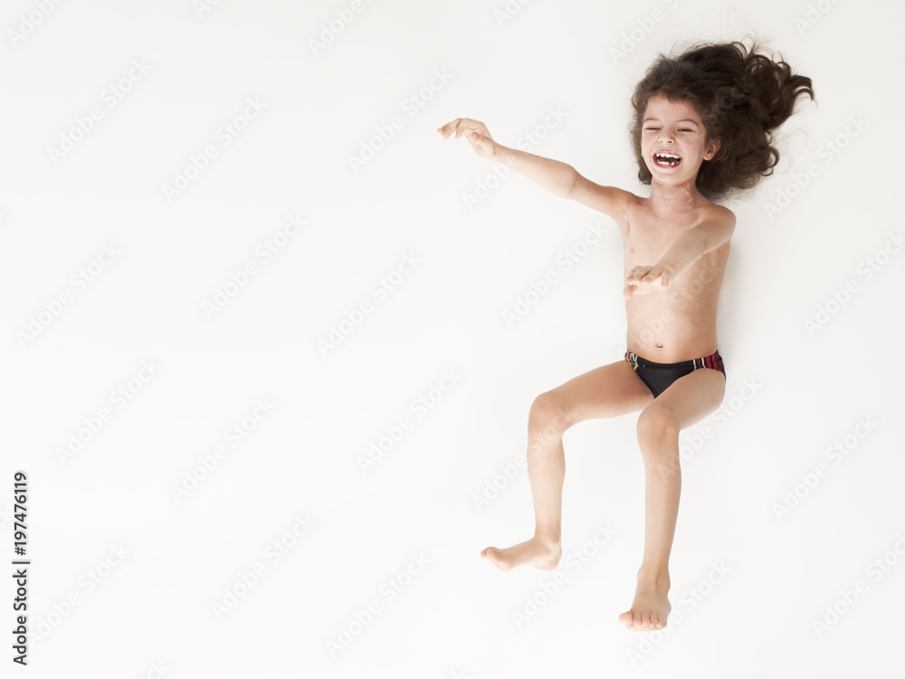 Smiling little boy in swimming trunks jumping with arms raised against a white background Smiling little boy in swimming trunks jumping with arms raised against a white background