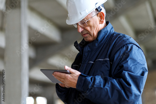 Senior construction manager controlling building site using digital tablet.