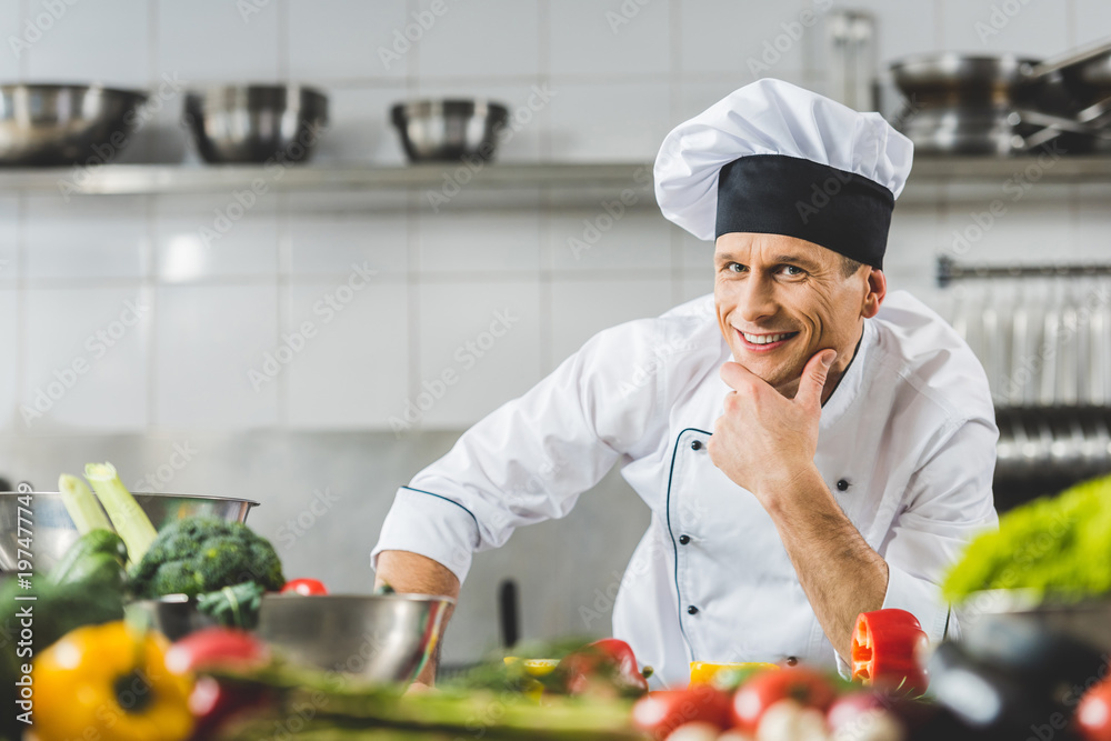 smiling pensive chef looking at camera at restaurant kitchen smiling pensive chef looking at camera at restaurant kitchen