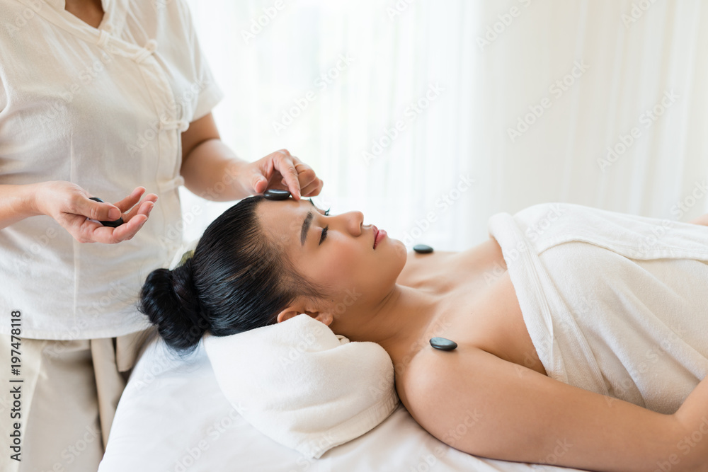 Young beautiful Asian woman relaxing having facial massage with mineral stone in the spa Young beautiful Asian woman relaxing having facial massage with mineral stone in the spa
