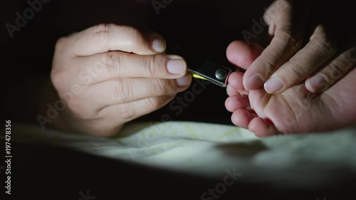 Mother hands are trimming baby foot nails at night