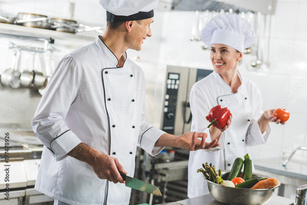 smiling chef giving red bell pepper to colleague at restaurant kitchen