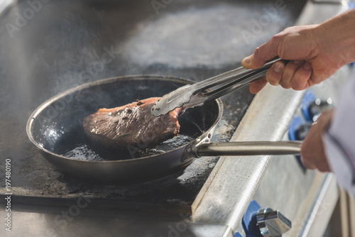 cropped image of chef frying steak at restaurant kitchen