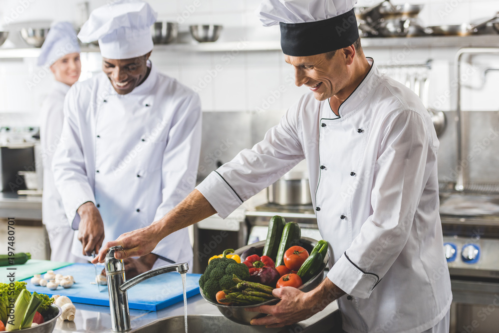 multicultural chefs cutting and washing vegetables at restaurant kitchen multicultural chefs cutting and washing vegetables at restaurant kitchen
