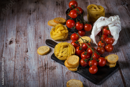 Fototapeta Naklejka Na Ścianę i Meble -  Red cherry tomatoes on wooden table with tagliatelle and bruschetta