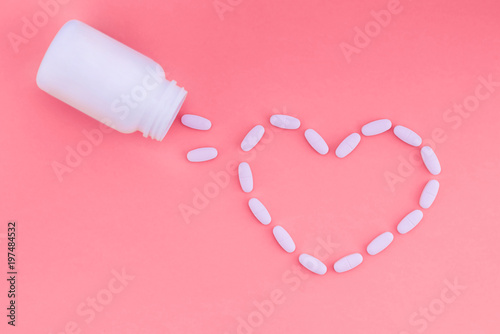 Heart of pills on a pink background. Tablets are strewn in the form of a heart from a white can of medicine. Flat lay.