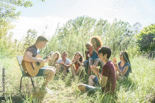 friends having fun playing guitar, singing, making music together  outdoors in the park on a weekend trip