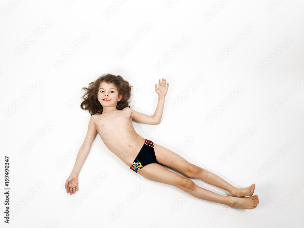Adorable little boy in a swimsuit lying on the floor, isolated on a light