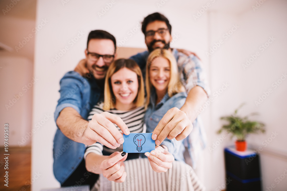 Group of happy charming young people holding together a small blue paper with a bulb for creative and innovative ideas. Group of happy charming young people holding together a small blue paper with a bulb for creative and innovative ideas.