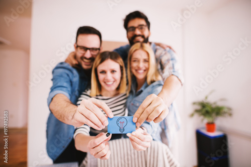 Group of happy charming young people holding together a small blue paper with a bulb for creative and innovative ideas.