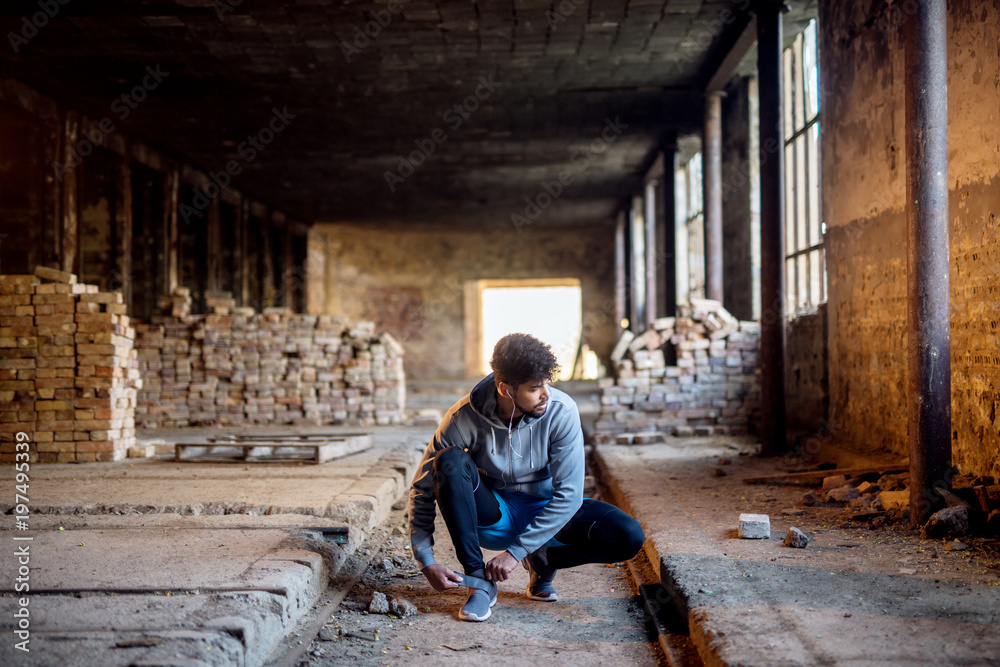 Close up view of sporty active afro american runner man crouching and tying velcro sneakers in the abandon place.