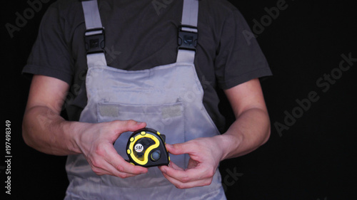 The master, builder or repairman holds in his hand a yellow tape measure of metrics, in a special suit, a black background.