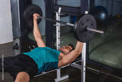 strong sportsman exercising with barbell in gym