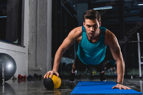 muscular sportsman doing push ups with medicine ball on yoga mat in sports center