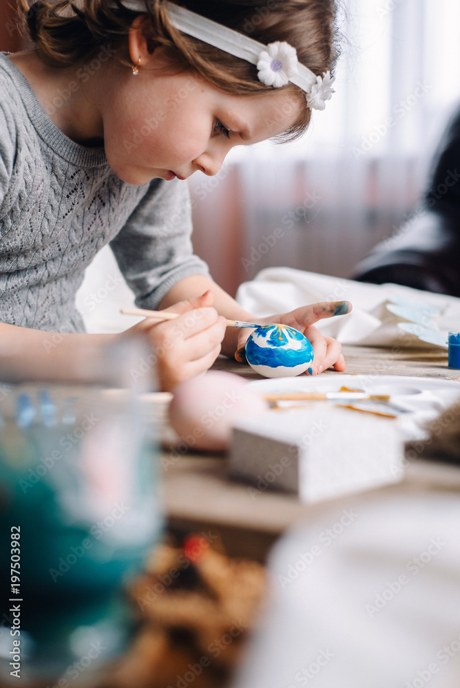 Happy easter! Cute little child girl painting with blue and yellow colors Easter eggs. family preparing for Easter