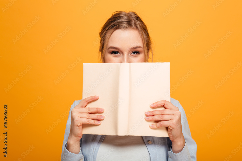 Happy young lady student covering face with book - obrazy, fototapety, plakaty 